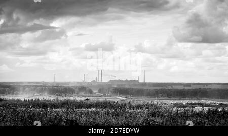 Silhouette d'une usine à l'horizon avec des cheminées fumage et des champs environnants contre un ciel nuageux, en noir et blanc Banque D'Images