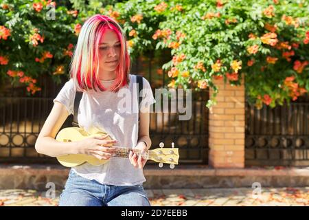 Hipster adolescent jouant ukulele assis à l'extérieur Banque D'Images