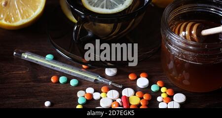 Médicaments et pilules sur une table en bois. Divers moyens pour prévenir les rhumes. Thé au citron et de miel. Tasse en verre avec plateau tranche de citron et un pot de miel. Banque D'Images