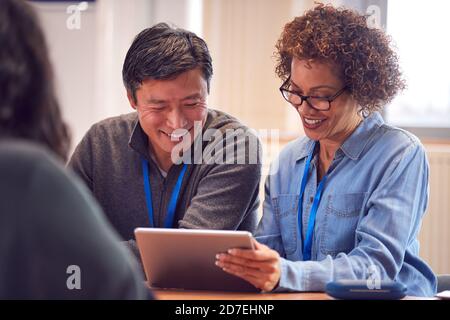 Professeur avec un étudiant adulte de sexe masculin mature utilisant une tablette numérique chez Table de travail dans la bibliothèque du Collège Banque D'Images