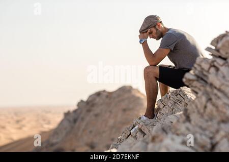Dépression et solitude. Triste jeune homme assis seul au sommet d'une falaise surplombant le désert. Banque D'Images