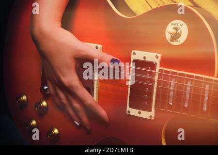 La main d'une femme avec une manucure se trouve sur le pont d'une guitare électrique rouge. Le guitariste joue de la musique dans le studio d'enregistrement. Banque D'Images