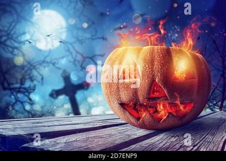 Citrouille sculptée souriante d'halloween avec feu dans un cimetière Banque D'Images