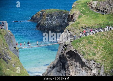 Les touristes traversent le pont de corde Carrick-a-Rede, un pont suspendu sur la côte d'Antrim en Irlande du Nord, au Royaume-Uni Banque D'Images