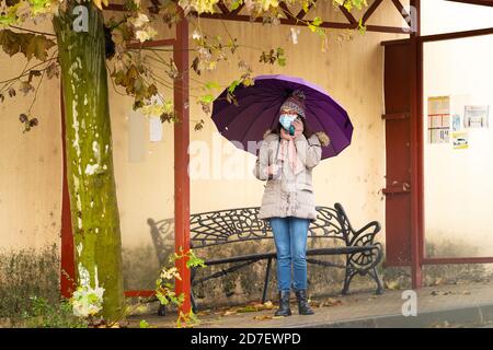 Femme avec parapluie à l'arrêt de bus parlant sur téléphone mobile Banque D'Images
