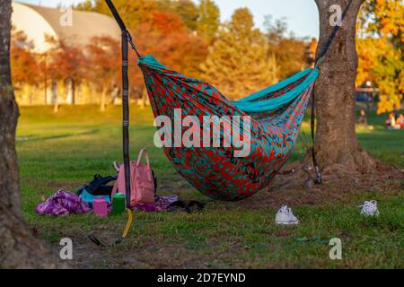 Une scène d'automne dans un parc avec un hamac coloré entre les arbres et quelqu'un dort dans lui. Un sac à dos rose, des baskets, des boissons en conserve sont scatte Banque D'Images