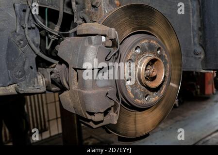 Ancien disque de frein avant avec étrier et plaquettes de frein dans la voiture, sur un ascenseur de voiture dans un atelier. Banque D'Images