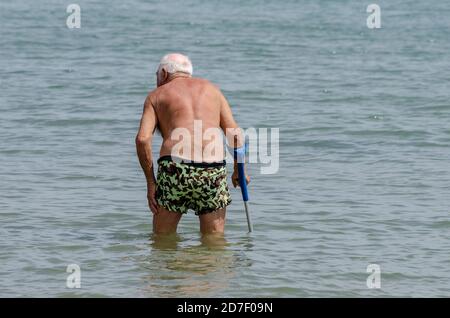 Un vieil homme à la mer marche et entre dans l'eau avec le bras Banque D'Images