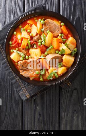 Ragoût épais de pommes de terre carottes pois langue et tomates gros plan dans un bol sur la table. Vue verticale du dessus Banque D'Images