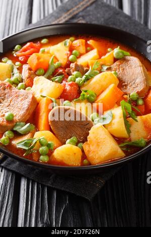 Ragoût épais de pommes de terre carottes pois langue de boeuf et tomates gros plan dans un bol sur la table. Vertical Banque D'Images