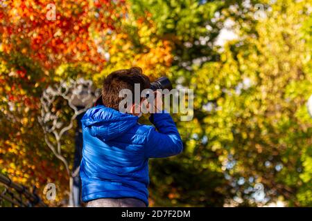 Un garçon caucasien portant un masque facial en raison de la pandémie de COVID-19 prend une photo du paysage d'automne à l'aide d'un appareil photo reflex numérique professionnel. Arbres colorés Banque D'Images