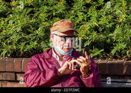 Frederick, MD, USA 10/14/2020: Un homme caucasien âgé essaie de composer un numéro sur le clavier de son vieux téléphone à clapet tout en tenant un cigare entre Banque D'Images