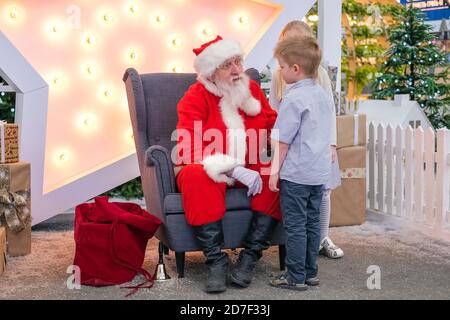 Le Père Noël parle et joue à des jeux surprise avec les enfants dans le centre commercial. Ventes et souhaits de Noël Banque D'Images
