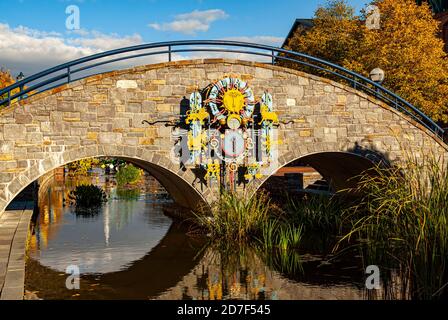 Frederick, MD, USA 10/13/2020: Un pont voûté en pierre pittoresque sur Carroll Creek avec des décorations métalliques sur le thème du zodiaque. Les feuilles d'automne tombent sur wat Banque D'Images