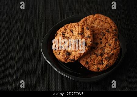 Biscuits aux pépites de chocolat faits maison dans une assiette noire. Touche Bas. Gros plan. Banque D'Images