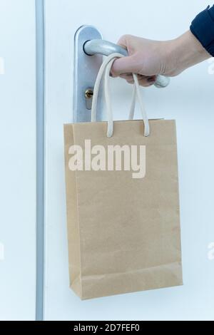 Une main humaine tente d'ouvrir une porte verrouillée et un sac en papier de nourriture est suspendu à son poignet. Livraison de nourriture sans contact. Commande de produits en ligne Banque D'Images
