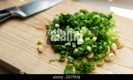 Poignée d'oignons verts frais finement hachés et couteau de cuisine sur bois, table rustique en bois. Gros plan de cuisson des légumes dans la cuisine.ingrédient Banque D'Images