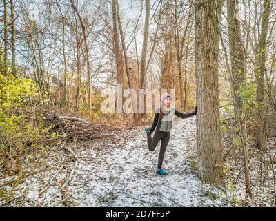 Hiver Running athlète femme sur la piste froide courir se préparer étirant jambes pour le jogging en dehors de la forêt séance d'entraînement porter des gants de vêtements chauds, hiver Banque D'Images