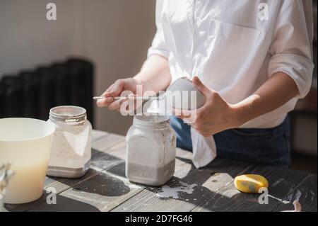 La femelle potter assis et agite la peinture avec un pinceau une tasse sur la table. Femme en céramique. Travail de poterie, compétences artisanales et créatives. Banque D'Images