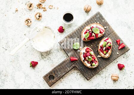 Sandwich avec fraises, fromage doux, noix, menthe et vinaigre balsamique sur bois sur fond gris. Vue de dessus. Banque D'Images