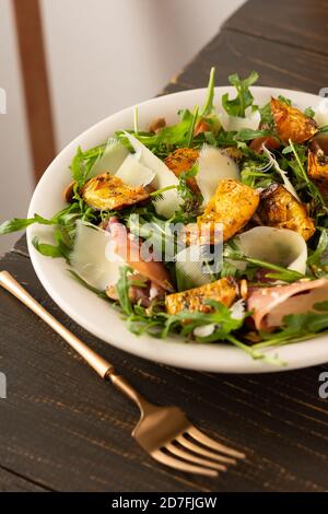 Salade automnale légère avec arugula, citrouille cuite, prosciutto et jeune parmesan, assiette de salade sur une table en bois Banque D'Images