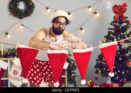 Elf ou Père Noël drôle dans le pantalon debout par ligne de sécher des chapeaux rouges dans sa maison décorée Banque D'Images