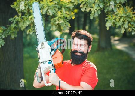 Bûcheron dans les bois avec hache à tronçonneuse. Beau jeune homme avec hache près de la forêt. Banque D'Images