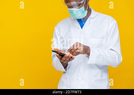 homme noir portant une blouse de laboratoire, et masque et écran nettoyant la surface de son téléphone Banque D'Images