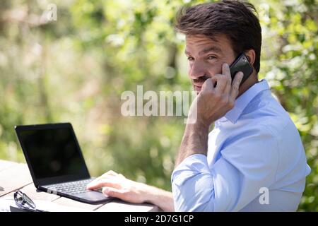 l'homme s'assoit sur un banc et utilise un pc et un téléphone Banque D'Images