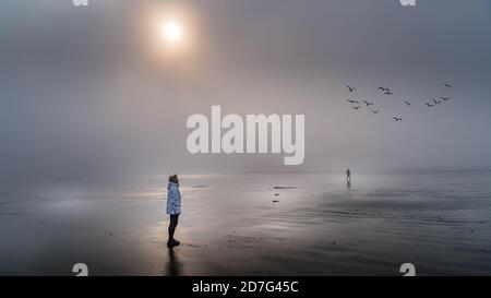 Femme âgée qui regarde dans le brouillard dense au-dessus de l'océan Pacifique à Cox Bay, dans le parc national Pacific Rim, sur l'île de Vancouver, en Colombie-Britannique, Banque D'Images