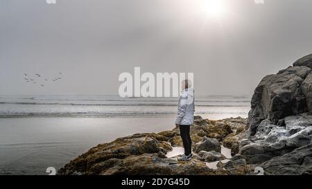 Femme âgée qui regarde dans le brouillard dense au-dessus de l'océan Pacifique à Cox Bay, dans le parc national Pacific Rim, sur l'île de Vancouver, en Colombie-Britannique, Banque D'Images