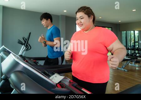 Deux asiatique entraîneur homme et femme de poids excessif entraînement sur tapis roulant dans la salle de gym. Les femmes grasses prennent soin de la santé et veulent perdre du poids. Banque D'Images