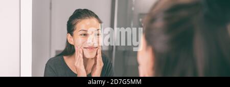 Visage laver jeune femme asiatique appliquer exfoliant peau dans Beauté soin de la peau routing matin style de vie - miroir de salle de bains bannière panoramique panorama Banque D'Images