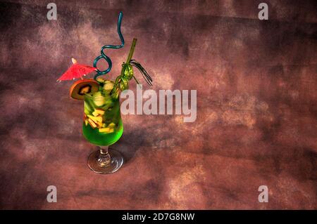 Grand verre de jus à base de kiwi avec glace, avec pailles et parapluie sur fond sombre. Gros plan. Banque D'Images