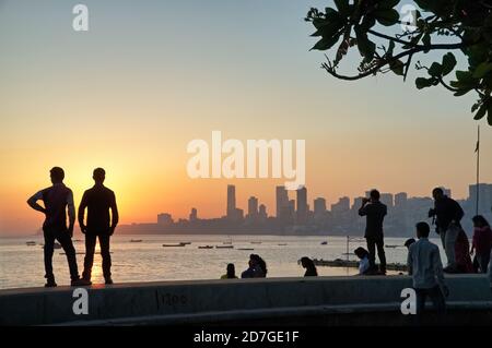 Pendant le coucher du soleil sur la mer d'Arabie à Marine Drive, près de Chowpatty Beach, Mumbai, les touristes locaux apprécient la vue tout en se tenant sur le remblai Banque D'Images