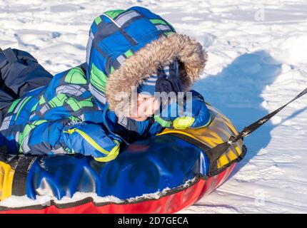 Un garçon en vêtements d'hiver fait un traîneau gonflable sur la neige blanche. Concept de jeux d'hiver en plein air. Banque D'Images