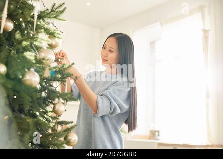 Jeune femme asiatique accrochant des boules de Noël sur l'arbre de Noël et préparation des vacances Banque D'Images