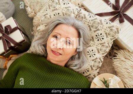 Vue en grand angle de la femme mûre qui s'est allongée sur un oreiller présente au repos et regarde la caméra Banque D'Images
