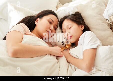 Mère asiatique dormant avec sa fille dans le lit dans la chambre Banque D'Images