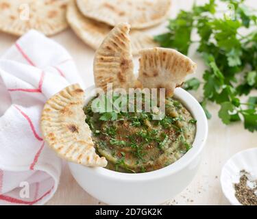 Trempez l'aubergine dans un bol en céramique blanc avec persil et pain plat à grains entiers sur fond de bois clair Banque D'Images