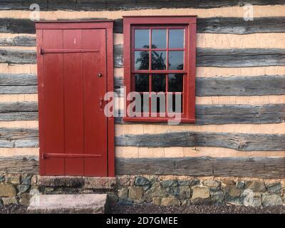 Porte rouge et ancienne fenêtre à 12 volets dans la cabane en rondins coloniale américaine. Banque D'Images