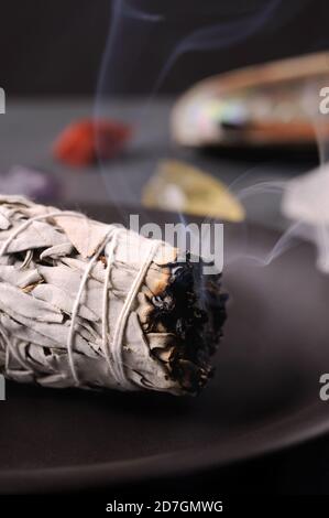 Rituel de saumuage utilisant un faisceau de sauge blanche brûlante à feuilles. Image avec pierres minérales de chakra curatif. Nettoyer la maison . Mise au point sélective. Banque D'Images