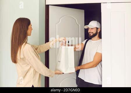 Jeune homme souriant messager donnant la commande dans le sac en papier à jeune femme cliente Banque D'Images