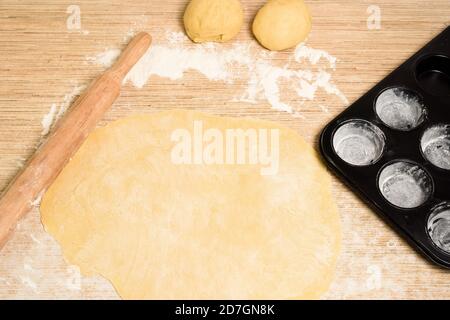 pâte roulée avec beurre sur la table avec une broche roulante pour les rouleaux et les rouleaux. à côté de elle est un moule à cupcake . la vue de dessus, place pour le texte. Banque D'Images