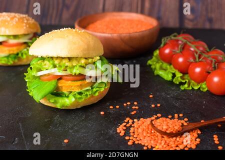 Hamburger végétarien avec tartelette, avocat, tomates, oignons, laitue sur une table en bois sur fond sombre. Délicieux Burger pour végétariens. Banque D'Images