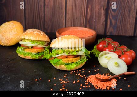 Hamburger végétarien avec tartelette, avocat, tomates, oignons, laitue sur une table en bois sur fond sombre. Délicieux Burger pour végétariens. Banque D'Images