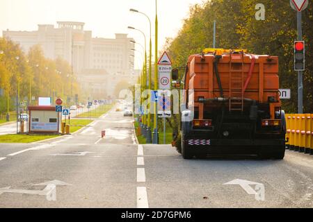 Vue arrière d'un camion lourd multifonction orange pour le nettoyage d'une rue en asphalte. La voiture se trouve à un carrefour le jour d'automne ensoleillé. Le travail Banque D'Images