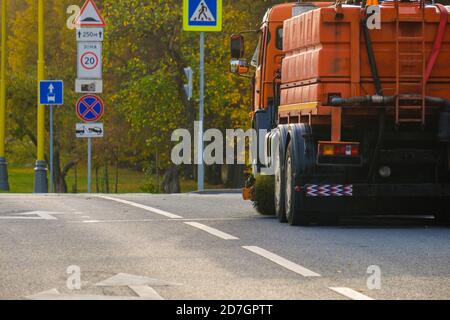 Vue arrière d'un camion lourd multifonction orange pour le nettoyage d'une rue en asphalte. La voiture se trouve à un carrefour le jour d'automne ensoleillé. Le travail Banque D'Images