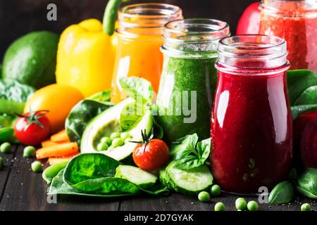 Jus de légumes végétaliens multicolores et smoothies de tomate, carotte, poivre, chou, épinards, betterave en bouteilles de verre sur table de cuisine rustique, ve Banque D'Images