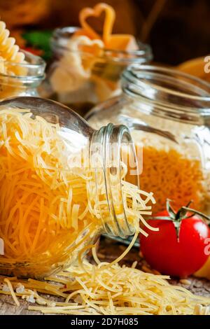 Faites sécher la fedelini italienne dans un pot en verre, mélange varié de différents types de pâtes, tomates cerises, persil sur le vieux fond en bois, sélectif Banque D'Images